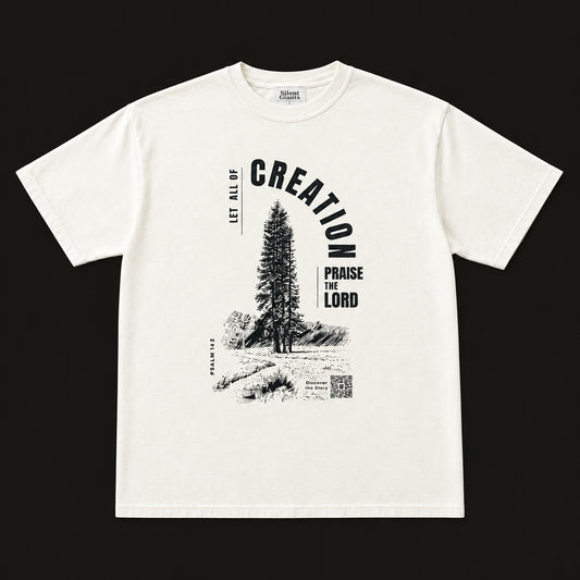 An off-white short-sleeve graphic t-shirt laid flat on an charcoal background. The shirt features a black graphic print of a pine tree and the words 'CREATION' and 'PARAGE FOR THE LORD'.