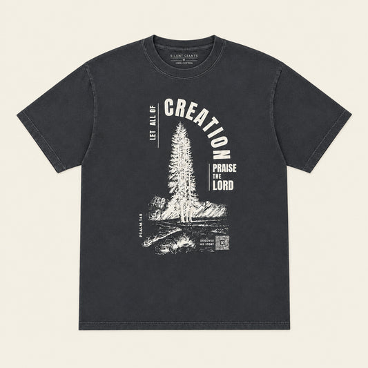 A dark charcoal gray graphic t-shirt laid flat on an ivory background. The shirt features a white distressed graphic of a pine tree with the text 'CREATION' arched above and 'PROVIDE FOR THE LORD' below.