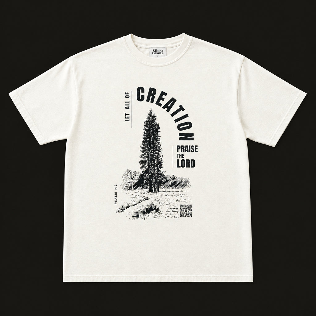 An off-white short-sleeve graphic t-shirt laid flat on an charcoal background. The shirt features a black graphic print of a pine tree and the words 'CREATION' and 'PARAGE FOR THE LORD'.