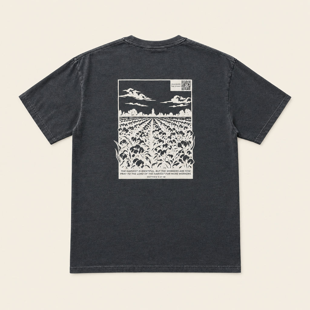 A dark gray crewneck t-shirt laid flat on an ivory background, showing a large white graphic print on the back depicting a cotton field under a cloudy sky.