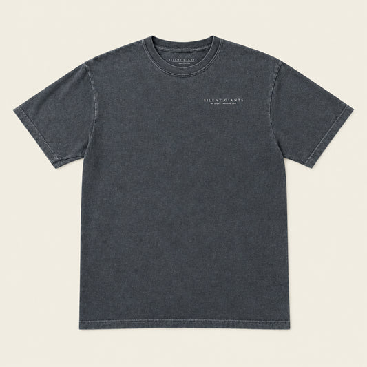 A dark gray crewneck t-shirt with 'Silent Giants above He Speaks through you.' printed in small white text on the left chest, laid flat on an ivory background.