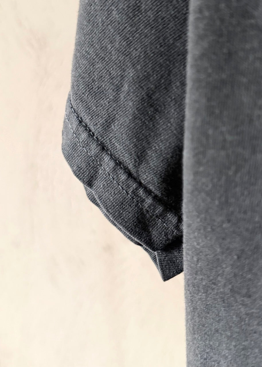 Close-up detail of a dark gray heathered fabric garment, showing a folded cuff with neat stitching against a light beige background.